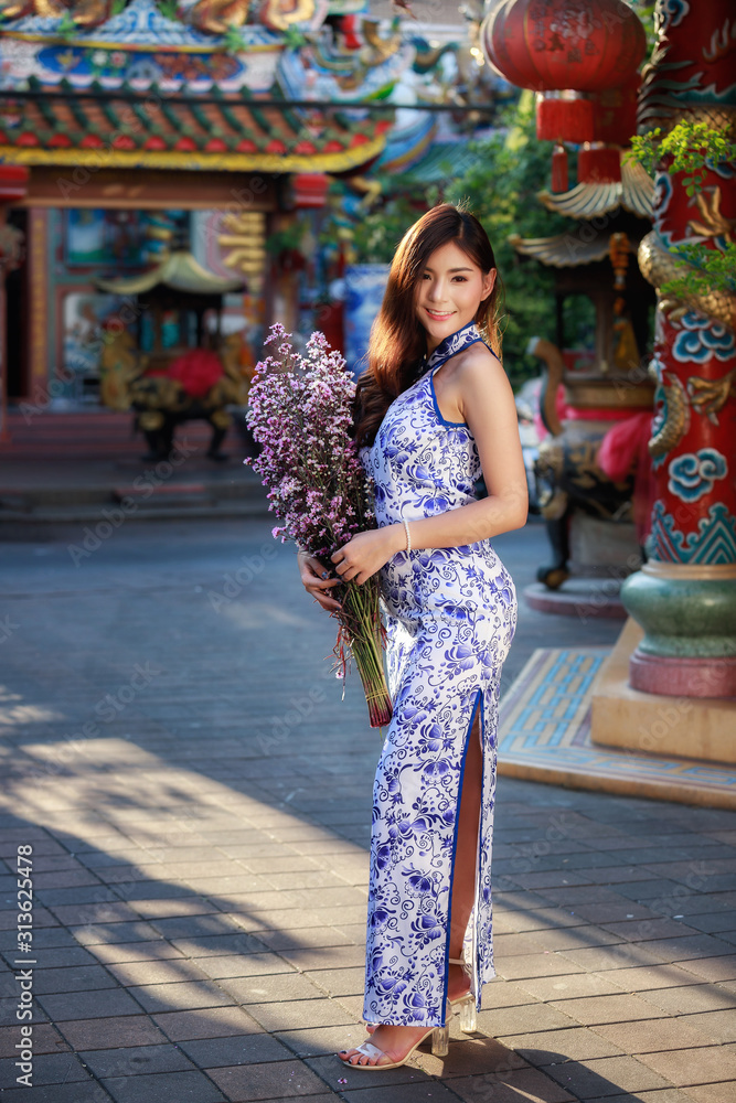 Chinese woman in cheongsam dress with a bouquet of flowers at shrine. Concept to celebrate Chinese New Year.