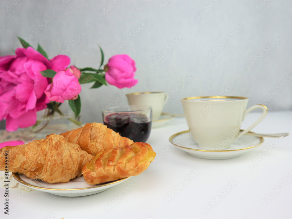 breakfast with two cups of coffee and croissants, bouquet of pink flowers breakfast with two cups of coffee and croissants, bouquet of pink flowers