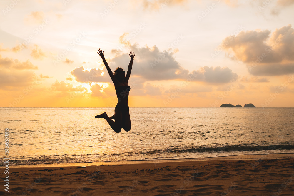 Silhouette of happy joyful woman jumping at the beach against the sunset