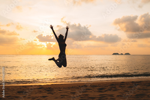 Silhouette of happy joyful woman jumping at the beach against the sunset