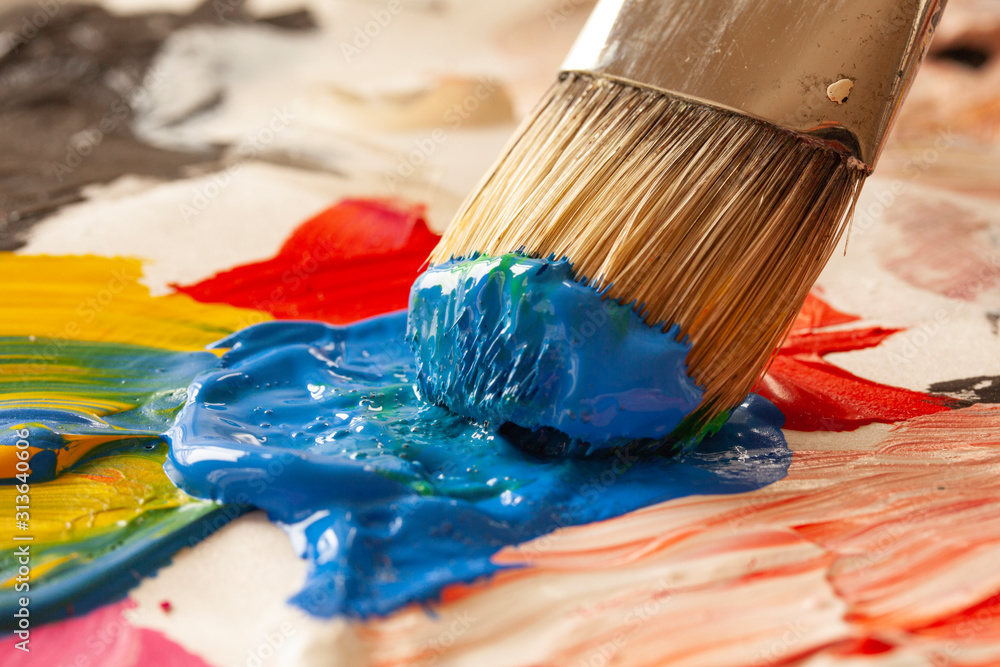 Fototapeta premium Close up of paintbrush picking blue color from an artist palette. Colorful image from an artist’s studio or a school showing creative education