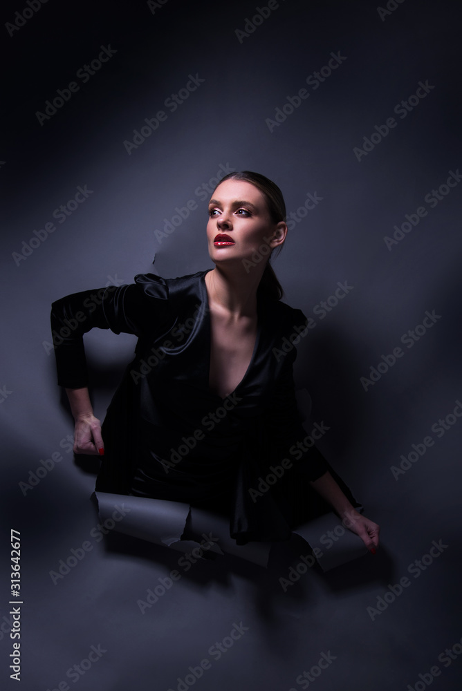 Vogue model posing in little black dress through wrapped paper grey background in studio, dramatic fashion poses, make up and hairstyle