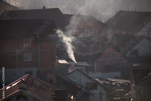 Smoking chimneys at roofs of houses emits smoke, smog at sunrise, pollutants enter atmosphere. Environmental disaster. Harmful emissions and exhaust gases into air. Fog, winter day, heating season.