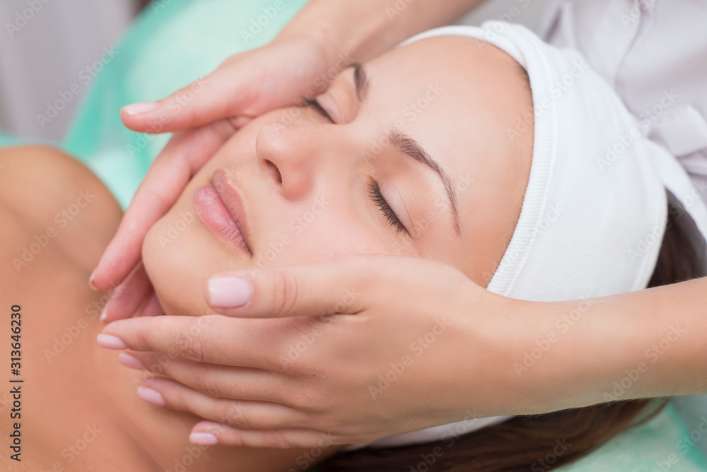 Girl massage therapist does facial massage with a beautiful woman. Hands are closing. Massage room