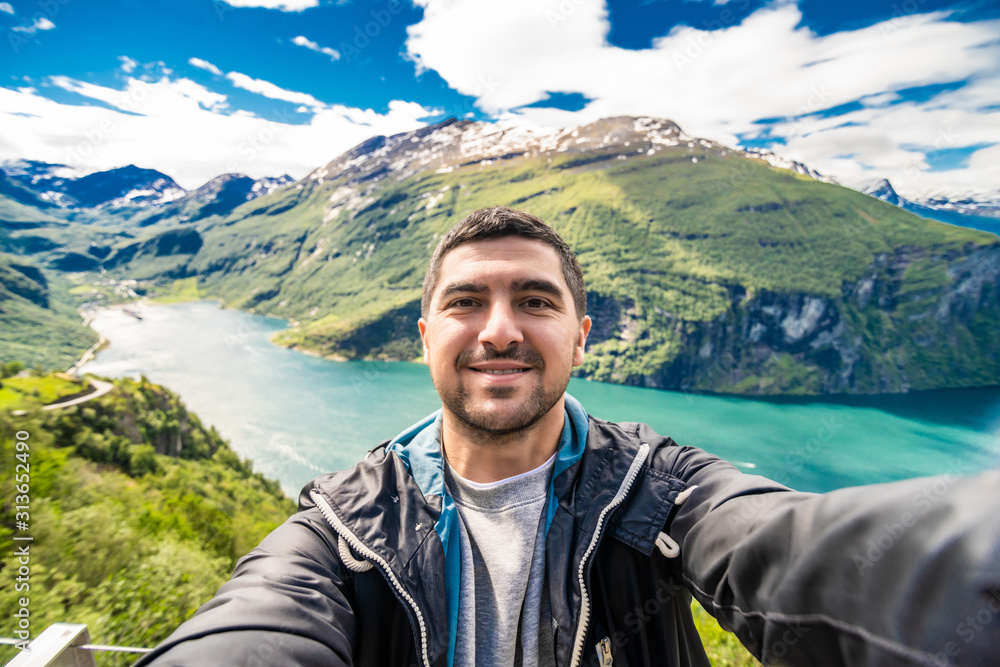 Young handsome man making selfie and relax on Geiranger fjord in Norway. Norway travel