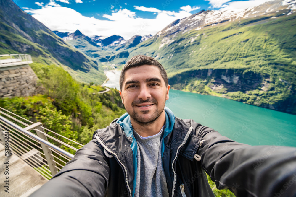Young handsome man making selfie and relax on Geiranger fjord in Norway. Norway travel