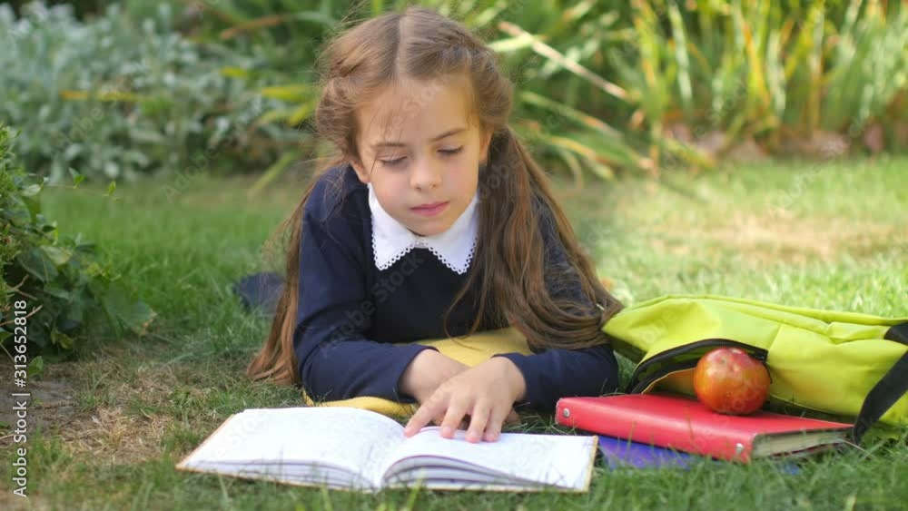 School. Girl schoolgirl lies on a lawn and reads a book. Children do homework. 4K UHD