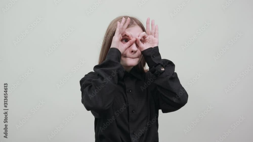 Crazy caucasian young woman in fashion black shirt isolated on gray background in studio doing okay gesture, glasses near eyes. People sincere emotions, lifestyle concept. Crazy caucasian young woman in fashion black shirt isolated on gray background in studio doing okay gesture, glasses near eyes. People sincere emotions, lifestyle concept.