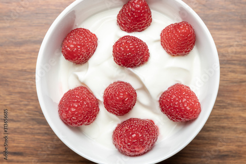 Cottage cheese with raspberries in a white bowl on a wooden table.