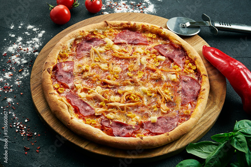 hawaiian Pizza with a large number of toppings: ham, pineapple, corn and chicken. Pizza in composition with ingredients on a black background