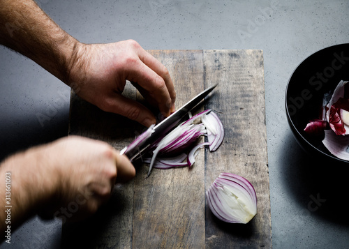 Overhead view of man's hands cutting onion on cutting board