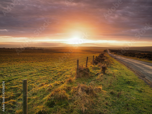 Beautiful sunset lighting up the clouds over Danby Moor with road and fence leading off into the distance, North York Moors National Park, UK