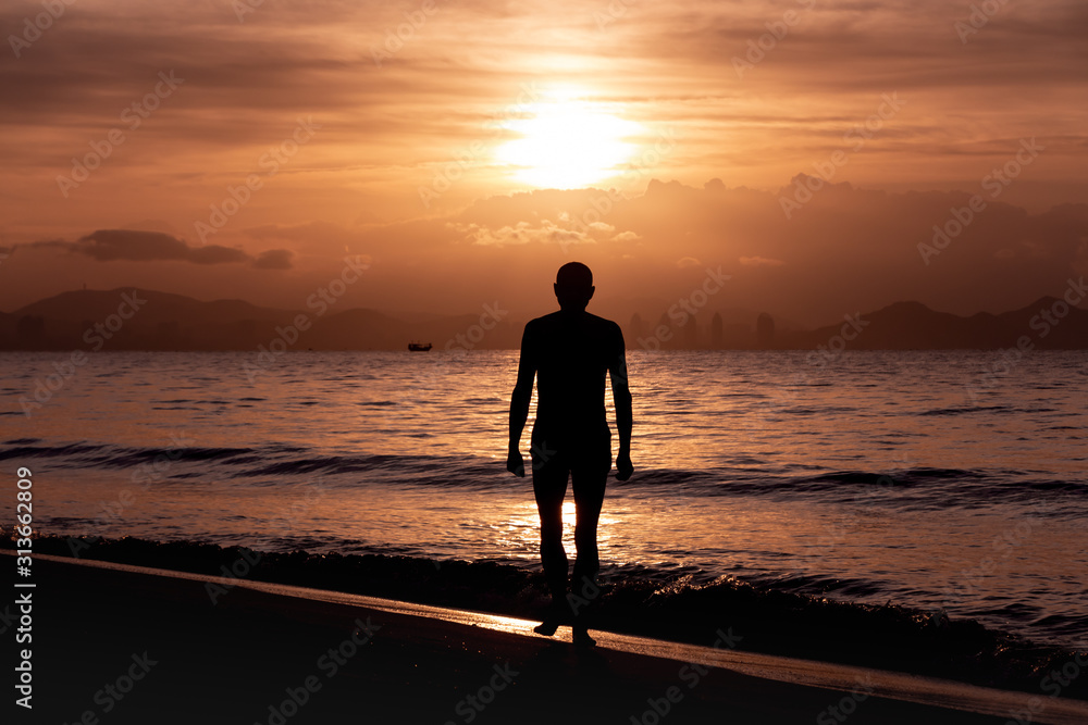 Man is doing his morning exercises on the beach during orange sunrise by the sea