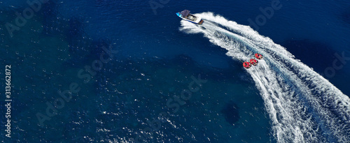 Aerial drone ultra wide photo of power boat towing children having fun with donut water-sports in deep blue Mediterranean bay © aerial-drone
