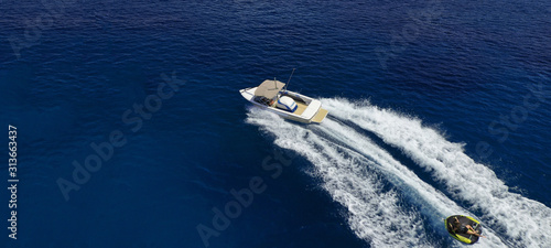 Aerial drone ultra wide photo of power boat towing children having fun with donut water-sports in deep blue Mediterranean bay © aerial-drone