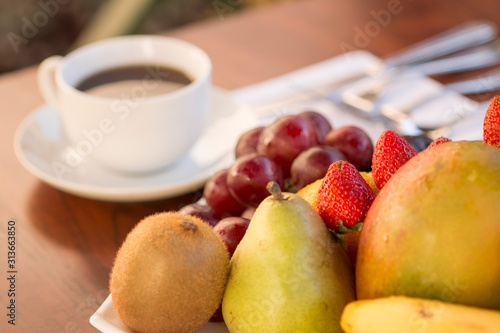 Fototapeta Naklejka Na Ścianę i Meble -  Colorful various fruits with white cup of coffee in the back over a wood table with natural light