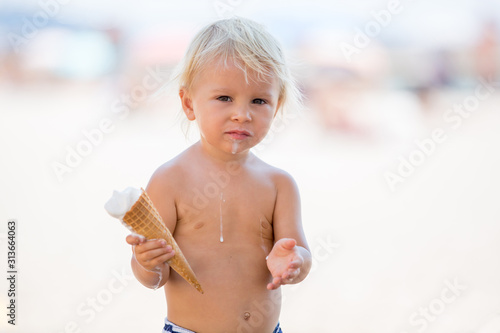 Sweet blonde toddler boy, eaiting ice cream on the beach photo