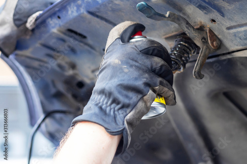 A man lubricates the hinges on the hood of a car