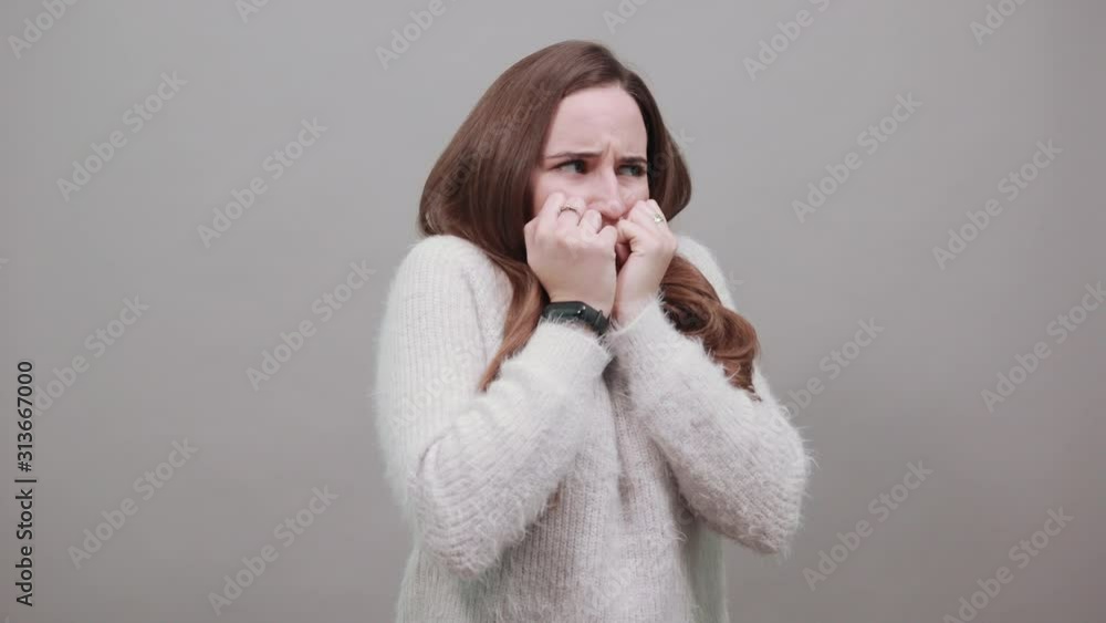 Scared attractive caucasian woman wearing nice clothes isolated on gray background in studio biting nails, keeping fists near mouth. People emotions, lifestyle concept. Scared attractive caucasian woman wearing nice clothes isolated on gray background in studio biting nails, keeping fists near mouth. People emotions, lifestyle concept.