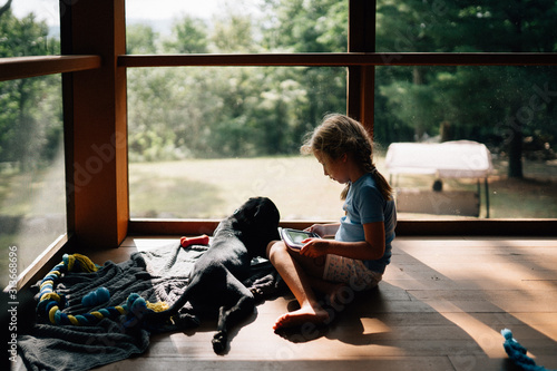 A little girl sits with her dog on a porch. photo