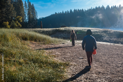 Two children walking in a meadow near a foggy lake at Sly Park photo