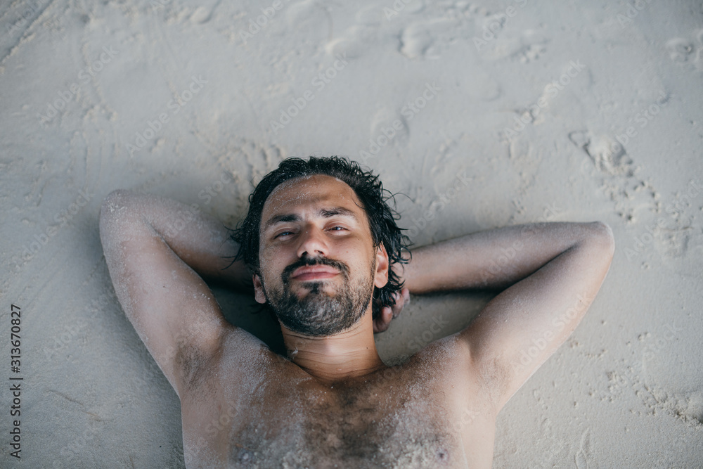 A handsome man lies on the sand by the ocean. A handsome man lies on the sand by the ocean.