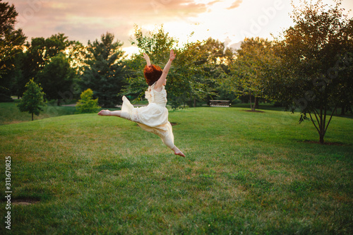 A joyful young dancer, lit by sunlight, leaps in a park at sunset