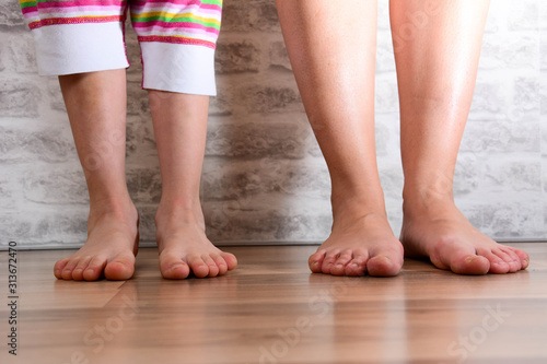 Healthcare concept. Beautifully groomed female feet on a white brick wall background. Child's feet on parquet laminate wooden texture floor close-up.