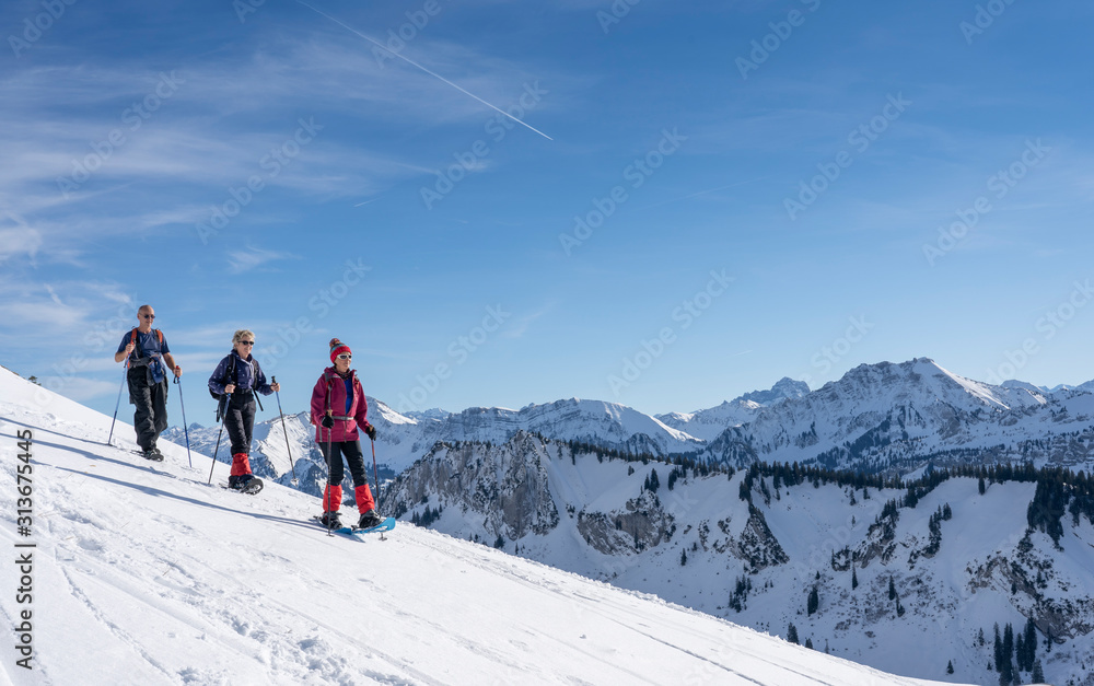 group of 3 senior adults snowshoeing  in the Bregenz wald mountains above the village of Bezau, Vorarlberg, Austria