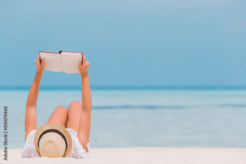 Fototapeta premium Young woman reading book during tropical white beach