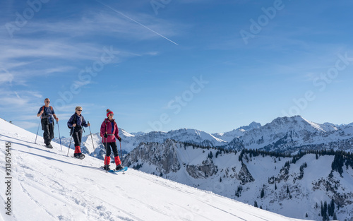 group of 3 senior adults snowshoeing in the Bregenz wald mountains above the village of Bezau, Vorarlberg, Austria