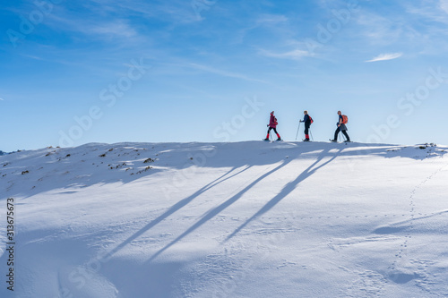 group of 3 senior adults snowshoeing  in the Bregenz wald mountains above the village of Bezau, Vorarlberg, Austria photo