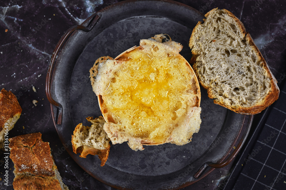 Baked and melted oven cheese in round wooden tray with fresh bread slices used to dip into cheese Baked and melted oven cheese in round wooden tray with fresh bread slices used to dip into cheese
