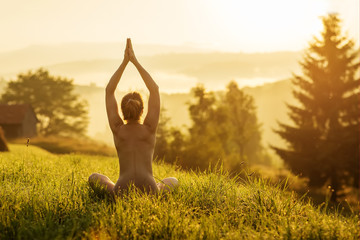 Nude woman practices yoga in nature