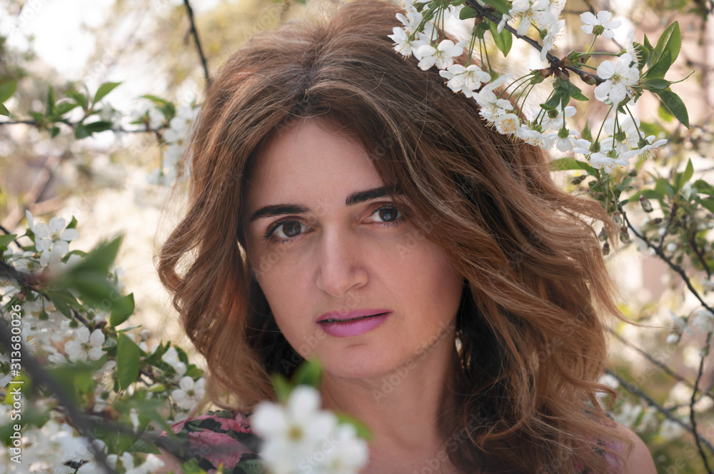 soft focus of portrait of attractive woman with long hair looking at camera surrounded by blooming cherry branches in garden soft focus of portrait of attractive woman with long hair looking at camera surrounded by blooming cherry branches in garden