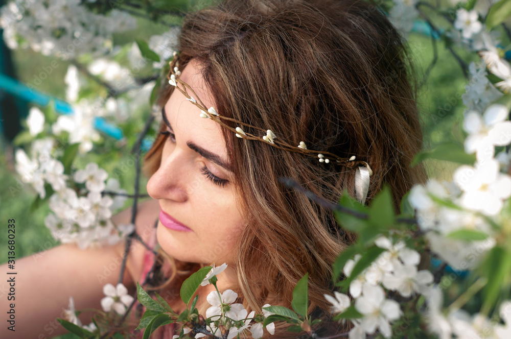 soft focus of portrait of attractive woman with long hair in wreath with tree branches looking away surrounded by white cherry blossom in garden soft focus of portrait of attractive woman with long hair in wreath with tree branches looking away surrounded by white cherry blossom in garden