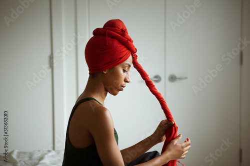 фотографія Woman twisting textile while tying headscarf at home