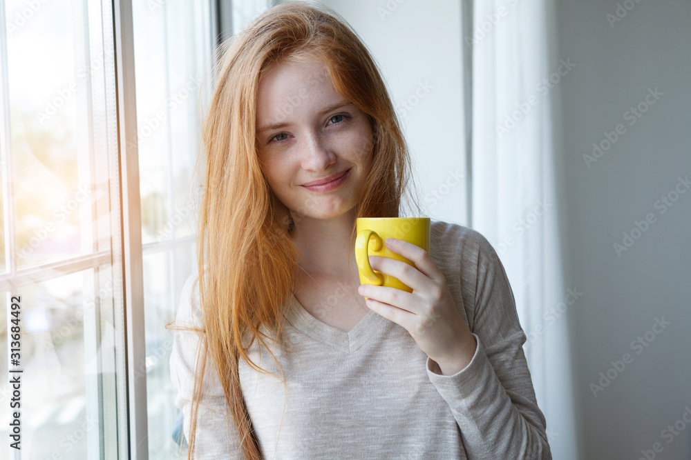 candid portrait of cheerful young smiling red hair woman holding yellow coffee cup, enjoying morning coffee and new day - obrazy, fototapety, plakaty 