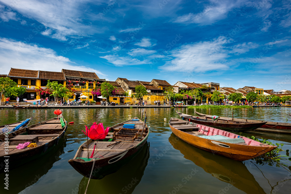 Fishing boats  on the Thu Bon River with old yellow buildings in Hoi An Vietnam