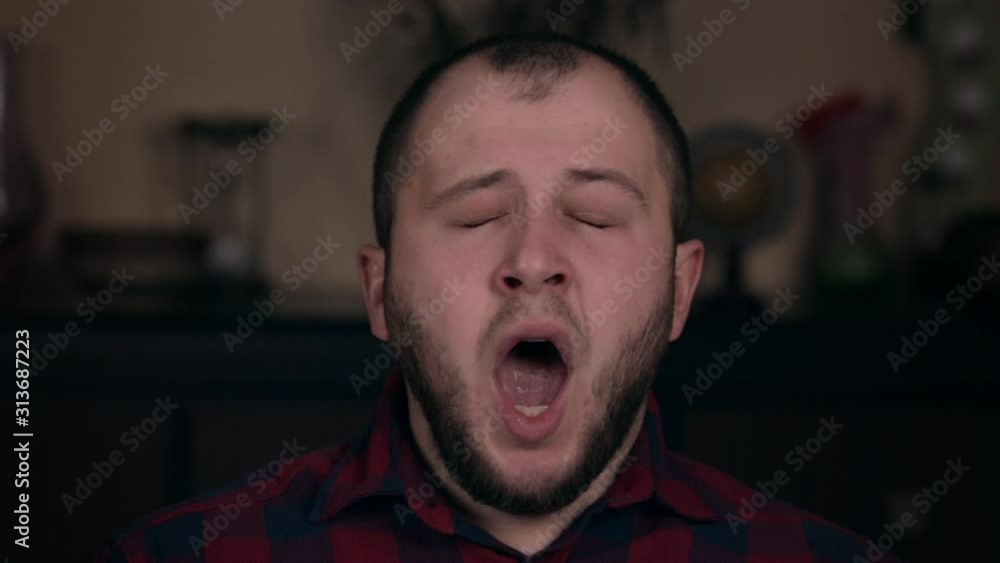A young guy of European appearance in a plaid shirt closeup yawns. The concept of emotions A young guy of European appearance in a plaid shirt closeup yawns. The concept of emotions