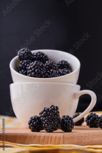 Three ripe fresh blackberries, close-up. Coffee cup filled with blackberries. black background.