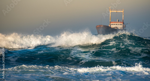Abandoned ship in the stormy ocean with big wind waves during sunset.