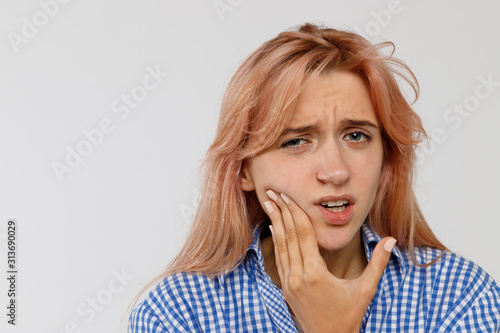 Teeth problem or dental illness. Young female feeling pain, holding his cheek with hand and suffering from bad tooth ache, isolated on grey background. Sensitive enamel concept