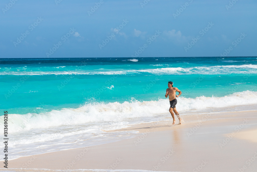 Junger Mann joggt an einem traumhaften Strand in der Karibik