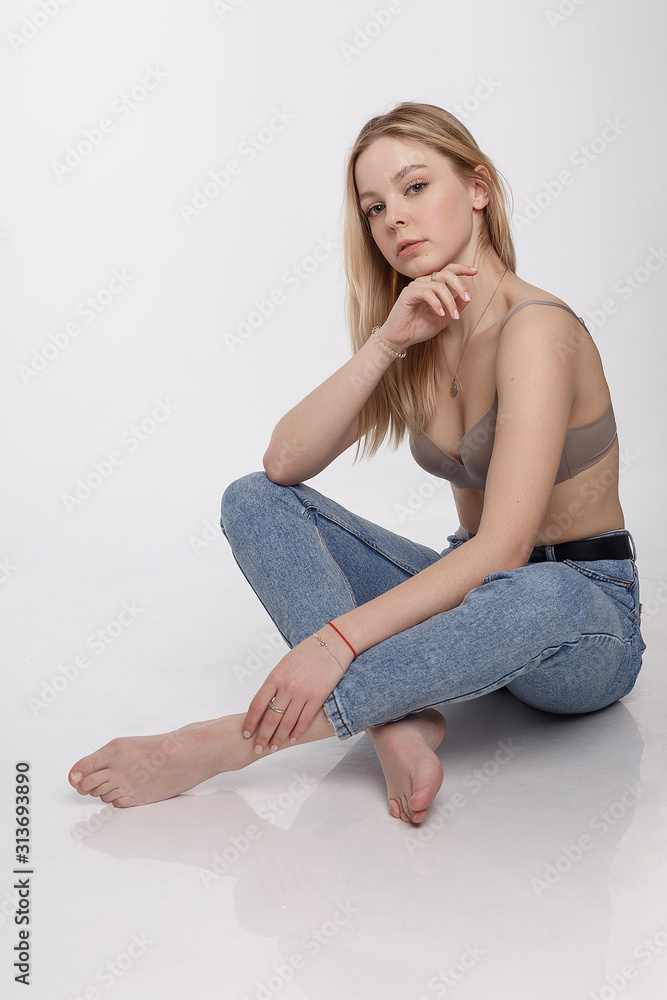 portrait of sexy caucasian woman with long hair posing in beige lingerie  and blue jeans on