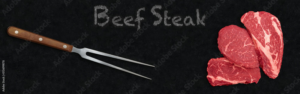 Uncooked red beef steaks for grilling on wide panoramic black stone cuisine table. Three striploin marbled black Angus steak, carving fork and chalk words - beef steak on black wide stone background.