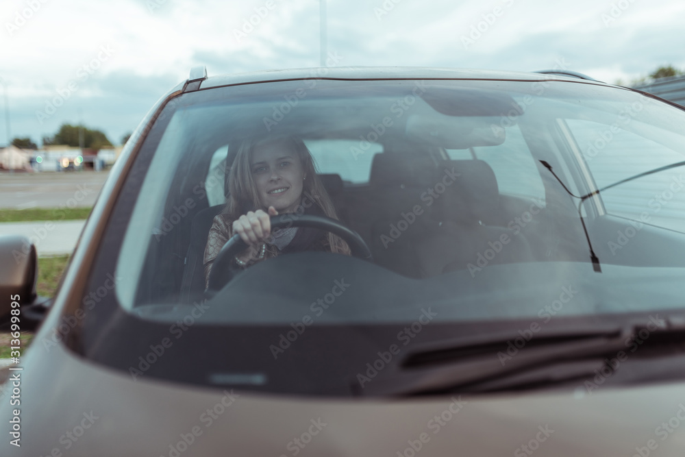 woman in car, sitting behind the wheel of a car, happy smile, right wheel of car, left-hand traffic. Windshield, fall day outside. Free space for copy text.