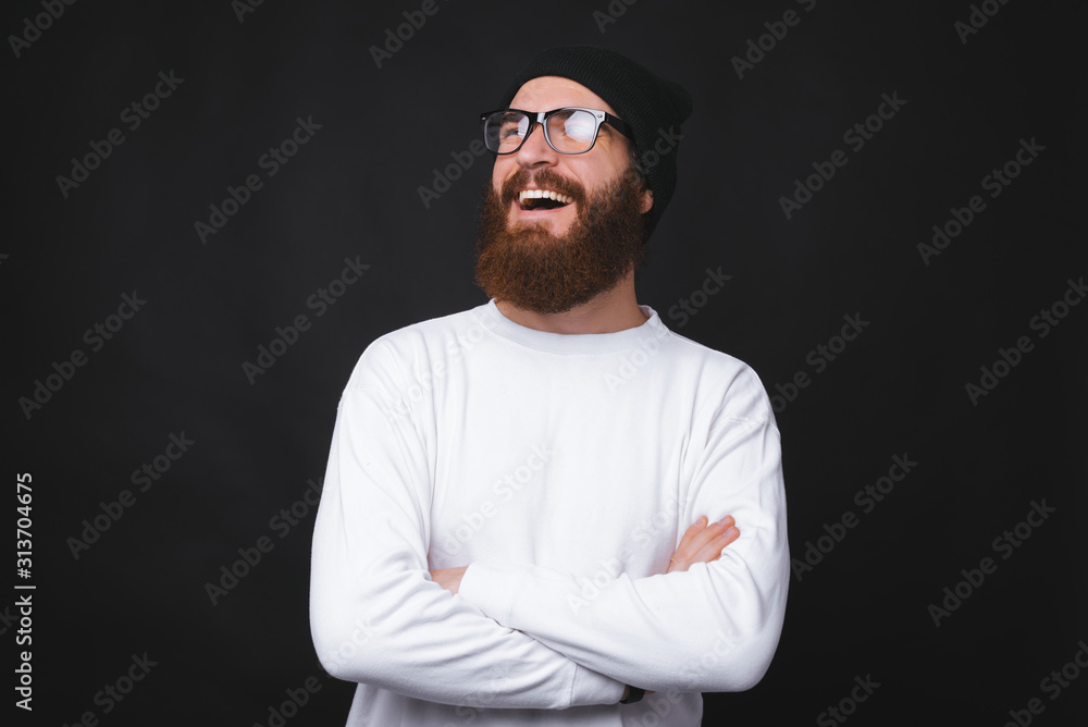 A young bearded man is smiling and standing with crossed hands on black background. A young bearded man is smiling and standing with crossed hands on black background.