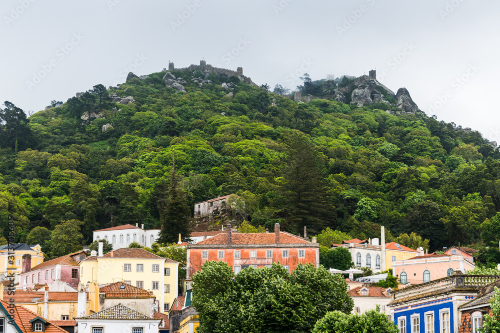 Beautiful village with colorful buildings on a forested hillside beneath misty castle battlements - Sintra, Portugal
