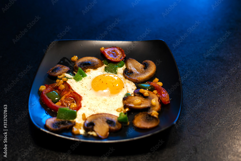 Freshly fried scrambled eggs with vegetables on a black plate